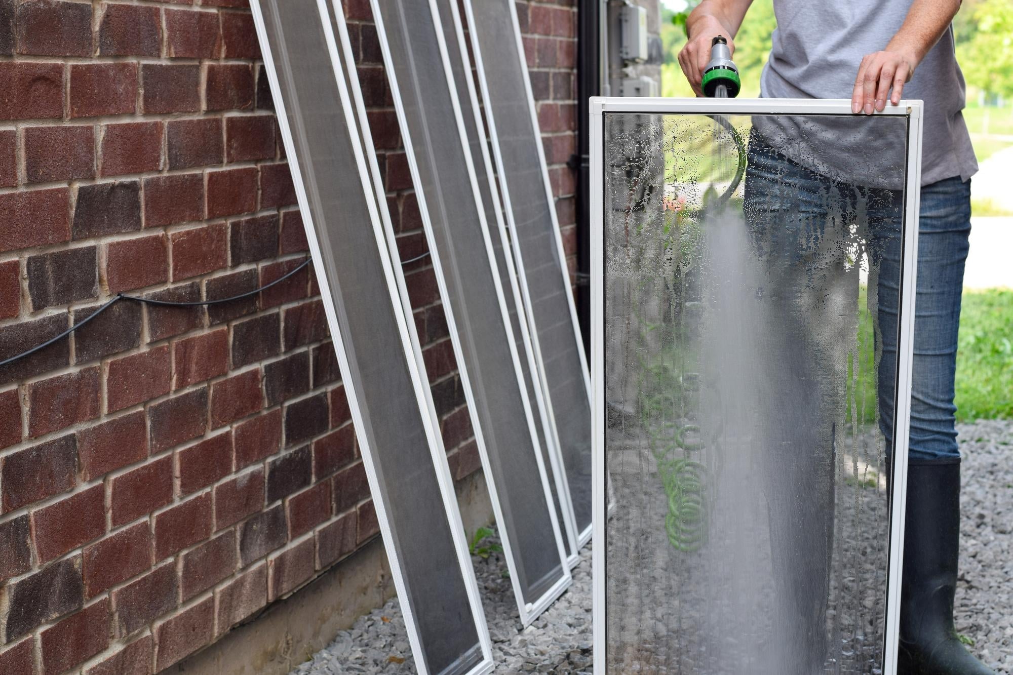 custom window screens woman cleaning window screens with water hose outside